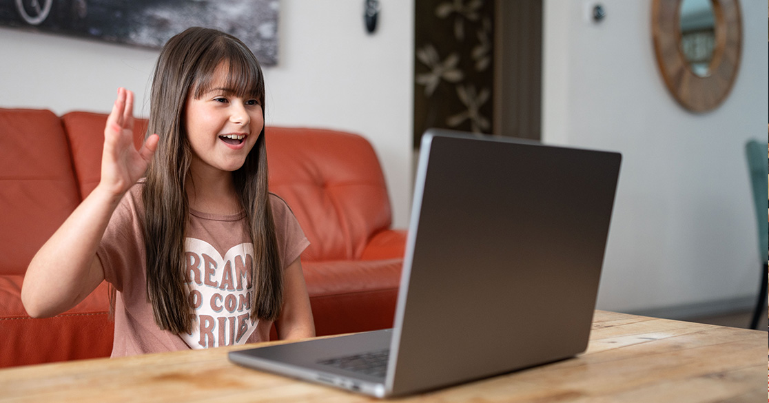 A girl sits in front of a laptop smiling while conversing with someone on the computer for her Florida Virtual School class.