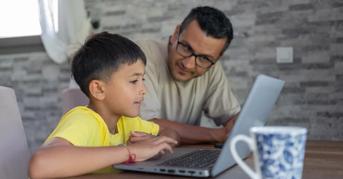 An adult and a child look at a laptop computer together at a table